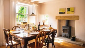 A dining room with a wooden table set for four, a fireplace, and two paintings on the wall.