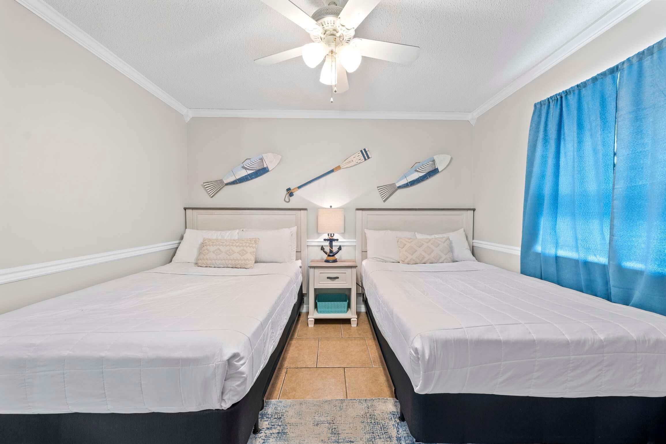 Une chambre avec deux lits, un ventilateur de plafond, une table de chevet avec une lampe et des décorations murales représentant des poissons.