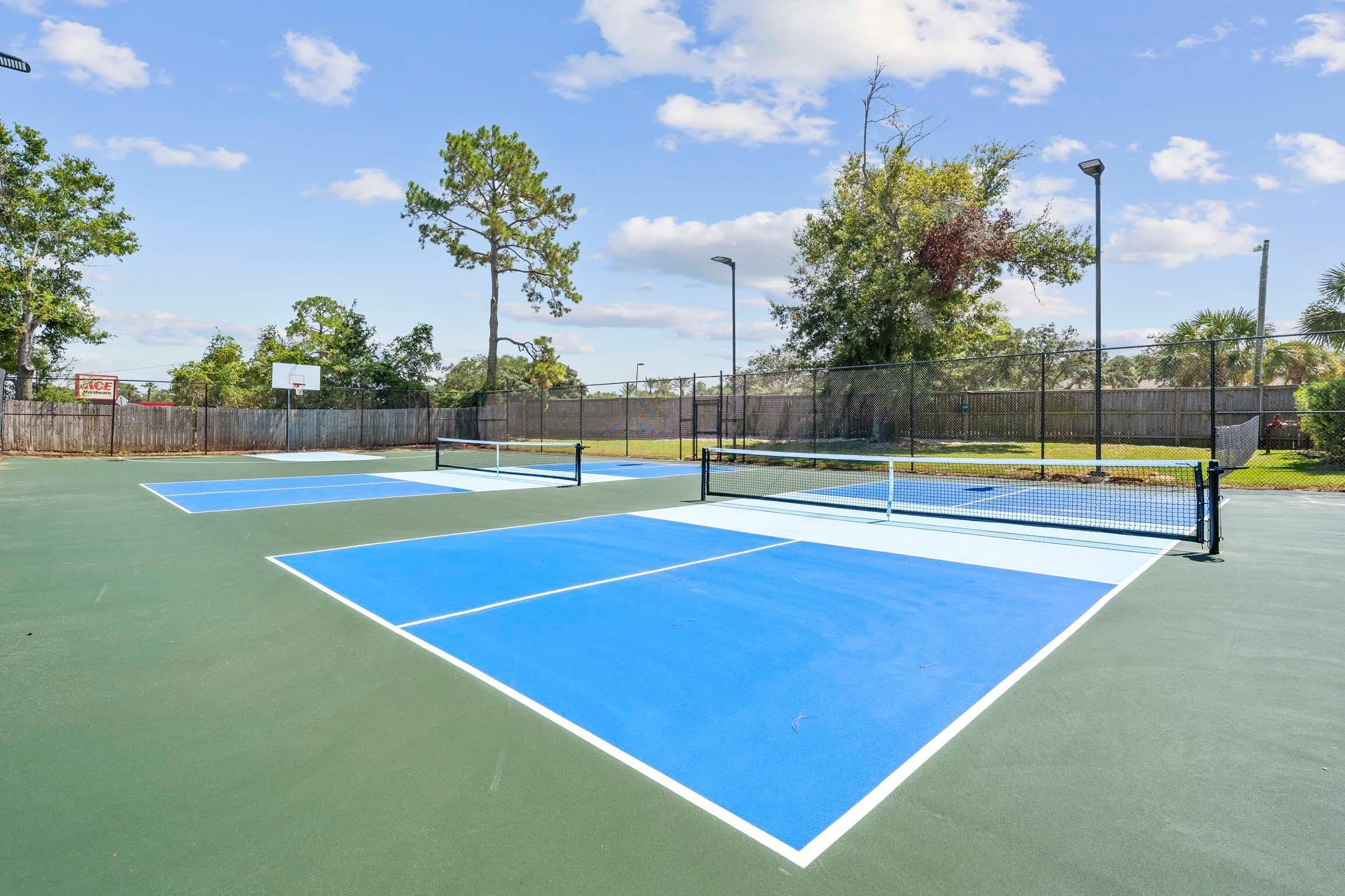 An outdoor tennis court with a net, surrounded by a fence and trees.