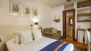 Un dormitorio con una cama grande, cabecera de madera, mesita de noche con lámpara, una silla y una pequeña mesa con un florero.