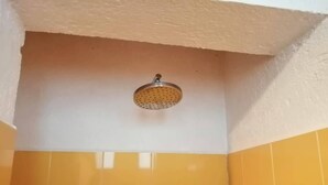 Rincón de un baño con azulejos amarillos y un cabezal de ducha.