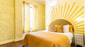 Una habitación con pared de ladrillo, una cama con cabecera amarilla y una mesita de noche.