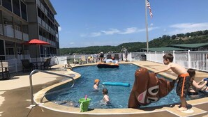 A swimming pool area with a pool float shaped like a bear, a flag, and a building with balconies.