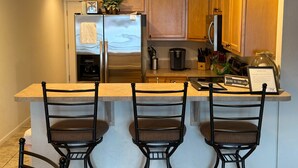 A kitchen with wooden cabinets, a stainless steel refrigerator, a coffee maker, and a sign that reads "Gone to the Lake".