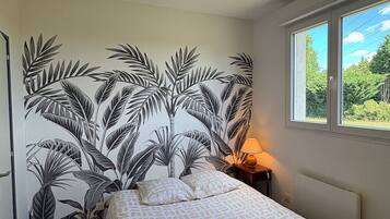 A bedroom with a bed, a nightstand, a lamp, a window, and a wall with a leaf pattern.