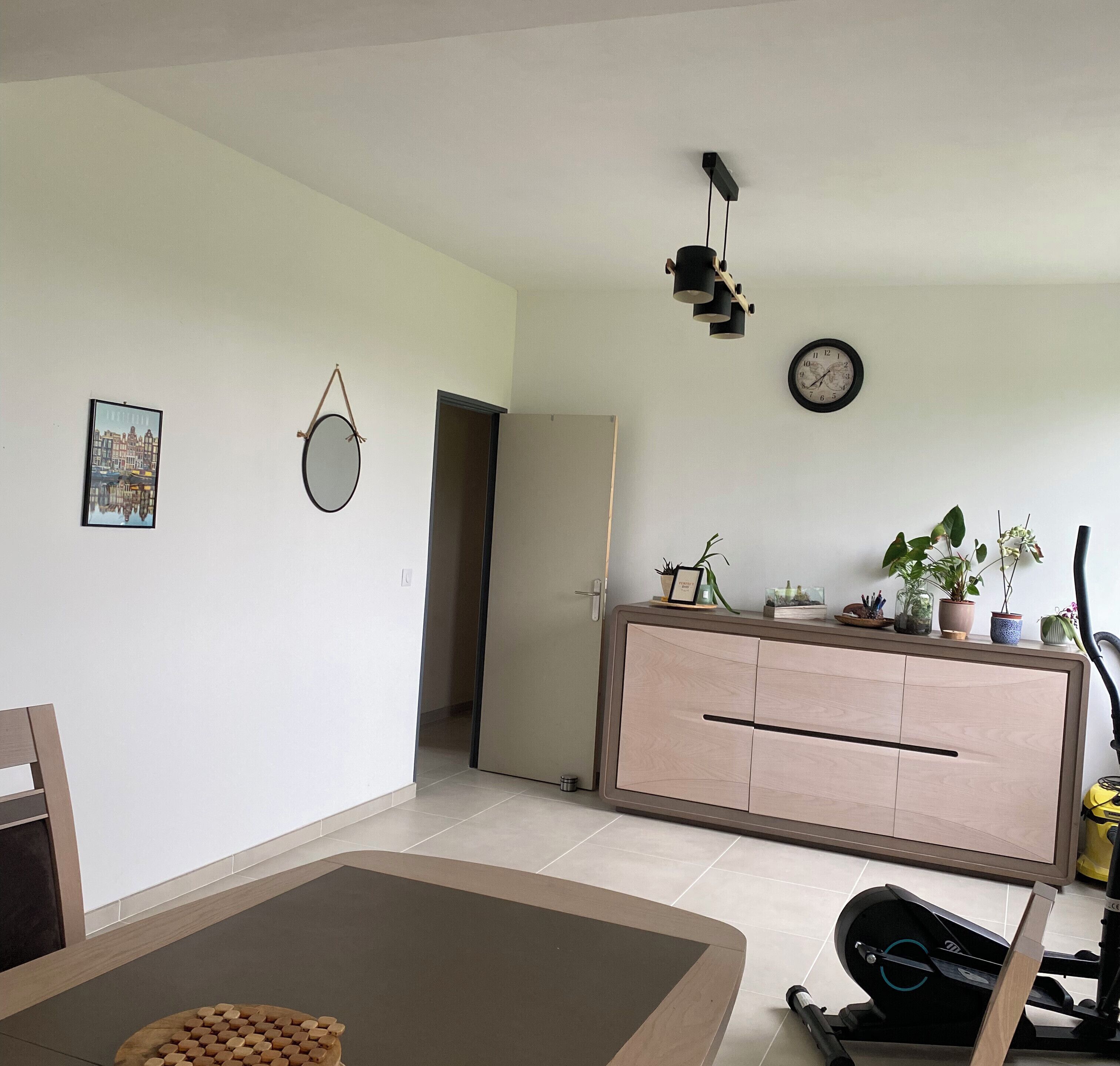 Ein modernes Wohnzimmer mit Essbereich, einer Couch, einem Couchtisch, einem Fernseher, einer Uhr und einem Topf mit Pflanze.