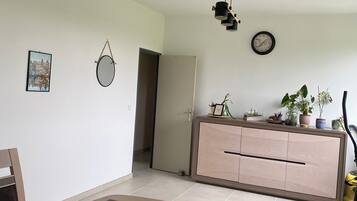Ein modernes Wohnzimmer mit Essbereich, einer Couch, einem Couchtisch, einem Fernseher, einer Uhr und einem Topf mit Pflanze.