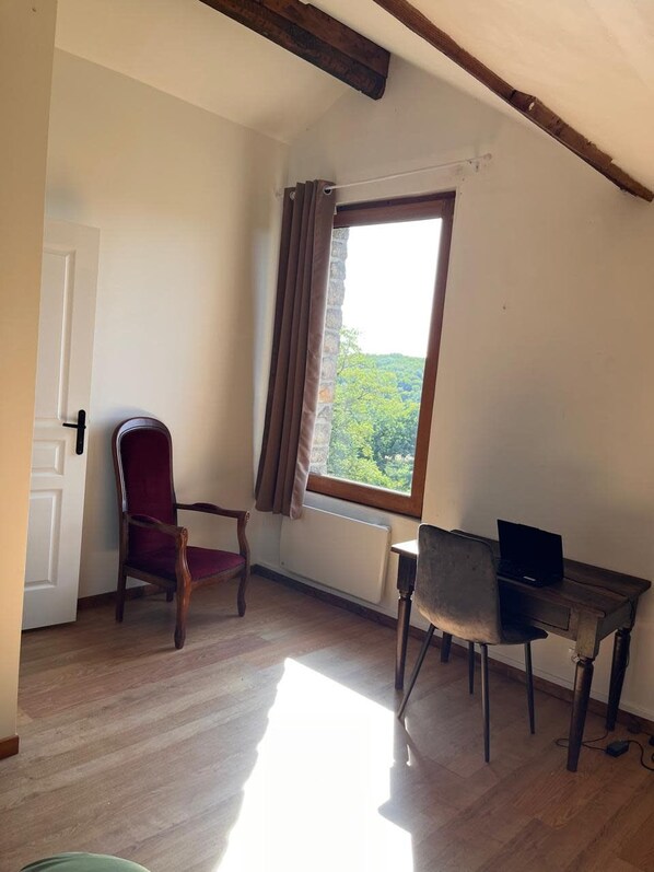 A room with a wooden floor, a red chair, a desk with a laptop, and a window with curtains.