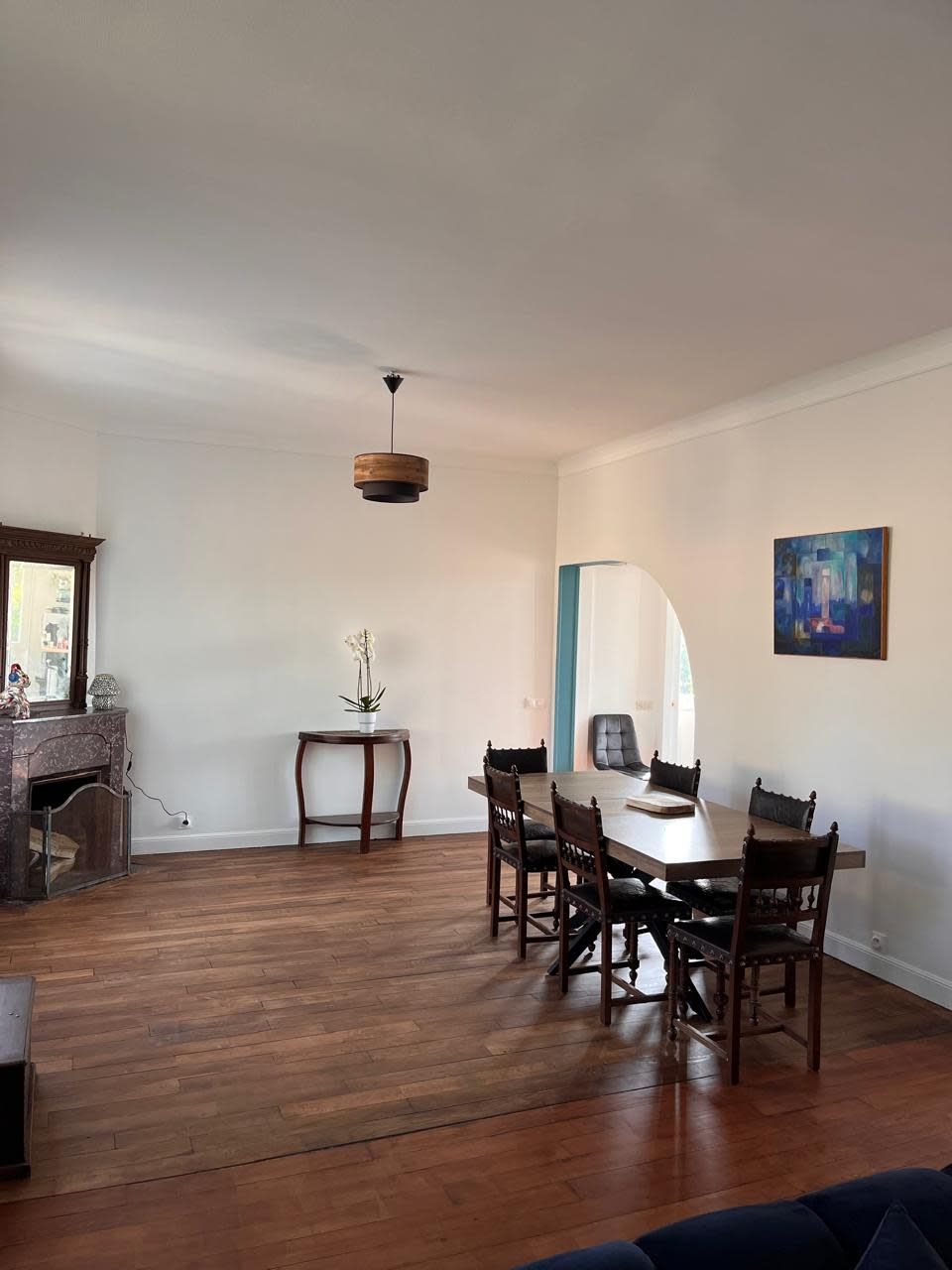 Un vaste espace dédié à la salle à manger, avec une table et des chaises en bois, un luminaire suspendu et un tableau accroché au mur.