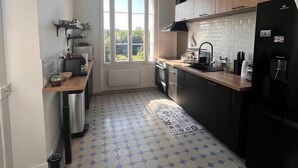 Una cocina con piso de baldosas, gabinetes de madera, un refrigerador negro y un ventanal con vista a la vegetación.