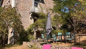 Una casa de piedra con balcón, mobiliario exterior y dos sillones rosados.