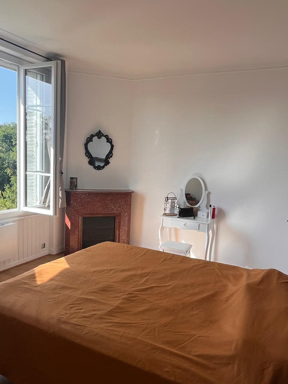 Une chambre à coucher avec un lit, une cheminée, une fenêtre et une commode avec un miroir.