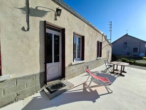 Um edifício com porta, janelas e um pequeno pátio com cadeira e mesa.