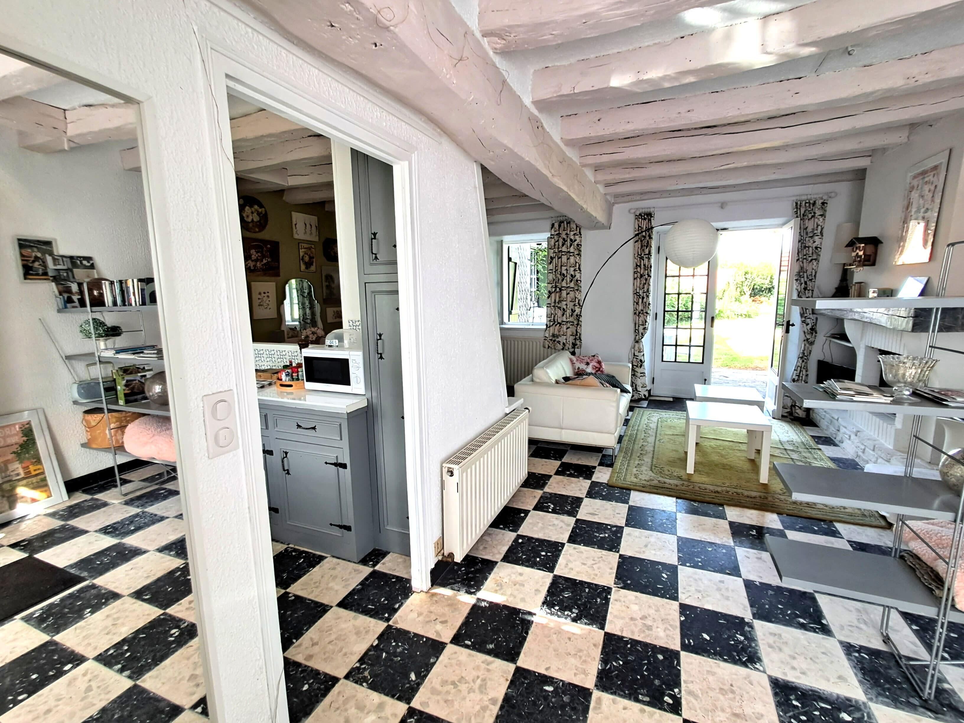 Una habitación con piso a cuadros, un sofá blanco, una mesa de comedor y una cocina con microondas.