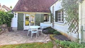 Una casa de campo pintoresca con un patio de piedra, una mesa blanca con sillas y una puerta verde.
