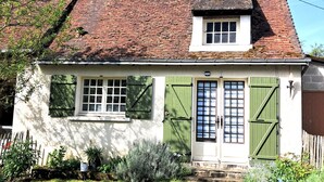 Una casa tradicional con techo inclinado, contraventanas verdes y un pequeño porche.