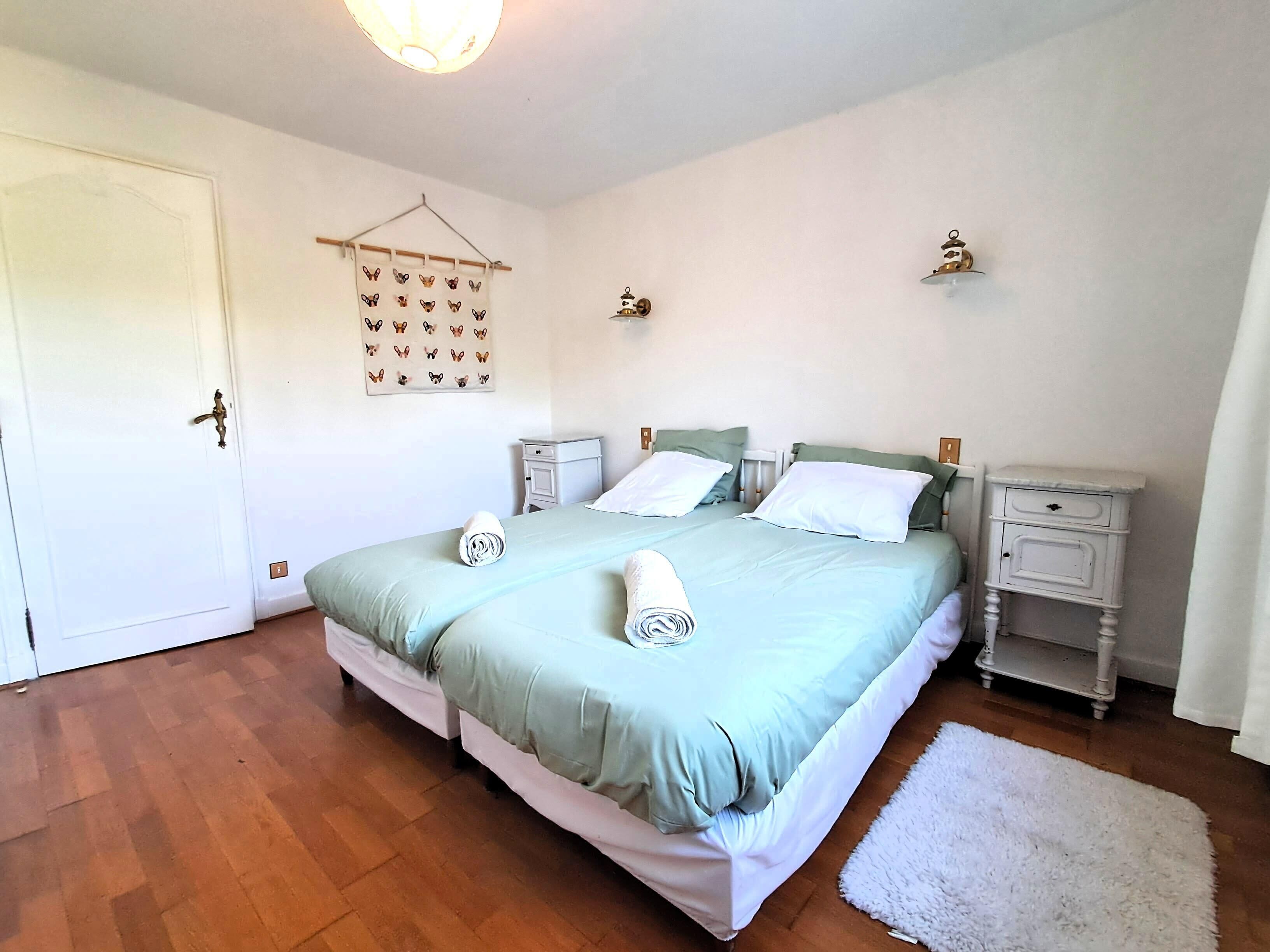 A bedroom with a double bed, two bedside tables, a hanging light fixture, and a white door.
