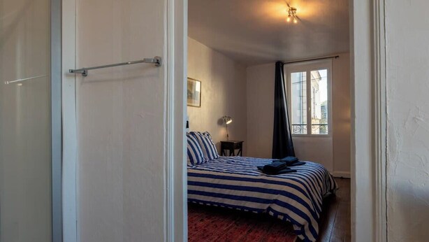 Une chambre à coucher avec un lit, une table de chevet, une lampe, une fenêtre avec des rideaux et une porte.