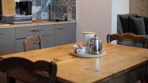 Une table à manger avec une cafetière, des tasses et des soucoupes, placée devant un mur décoré d’un motif et un meuble gris.