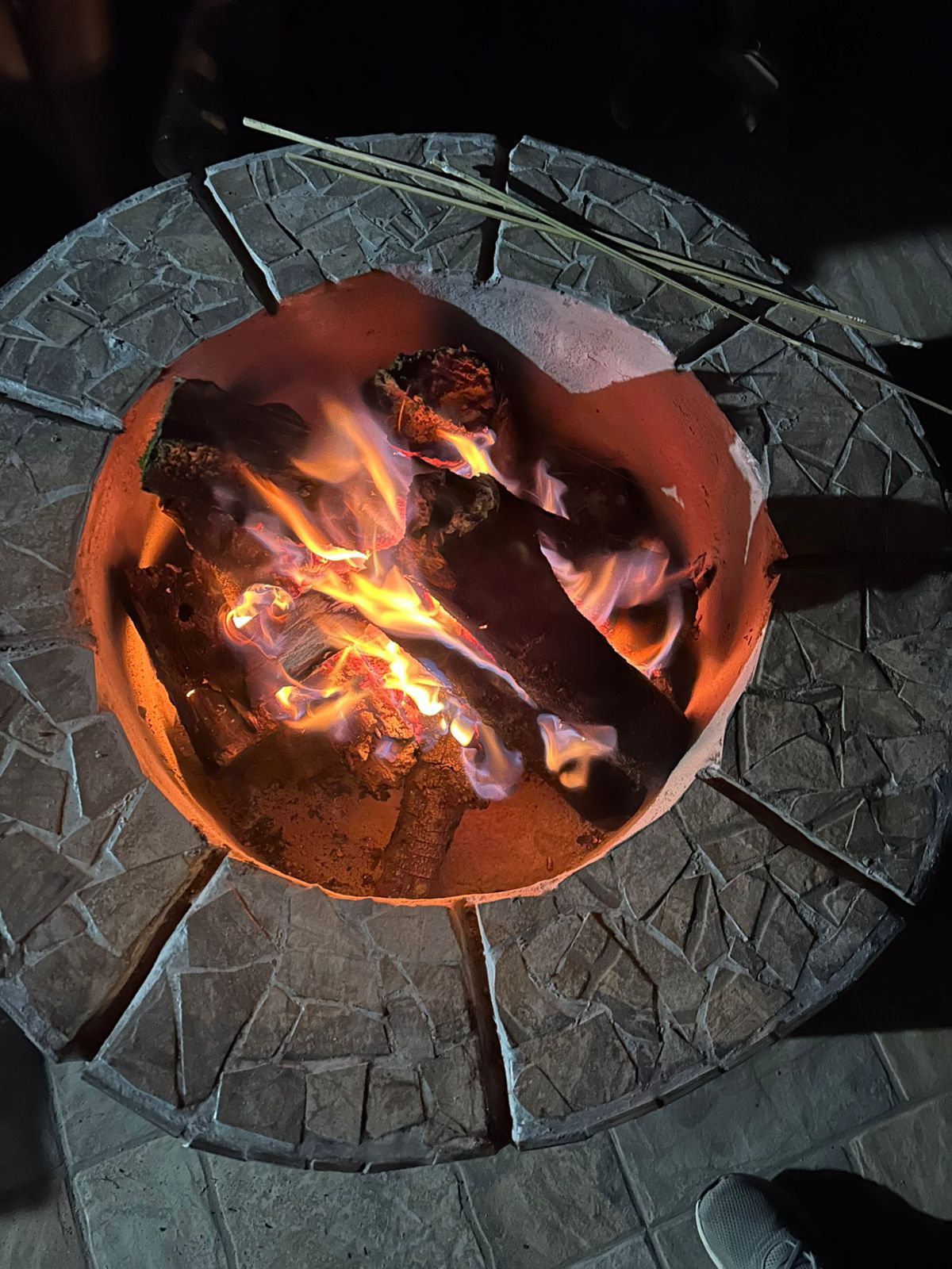 A circular fire pit with burning wood, surrounded by a stone-patterned floor.