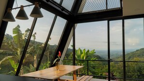 A room with a wooden table and bench, large windows offering a view of lush greenery and distant mountains. - AREWÁ Biohabitat (Pijao)