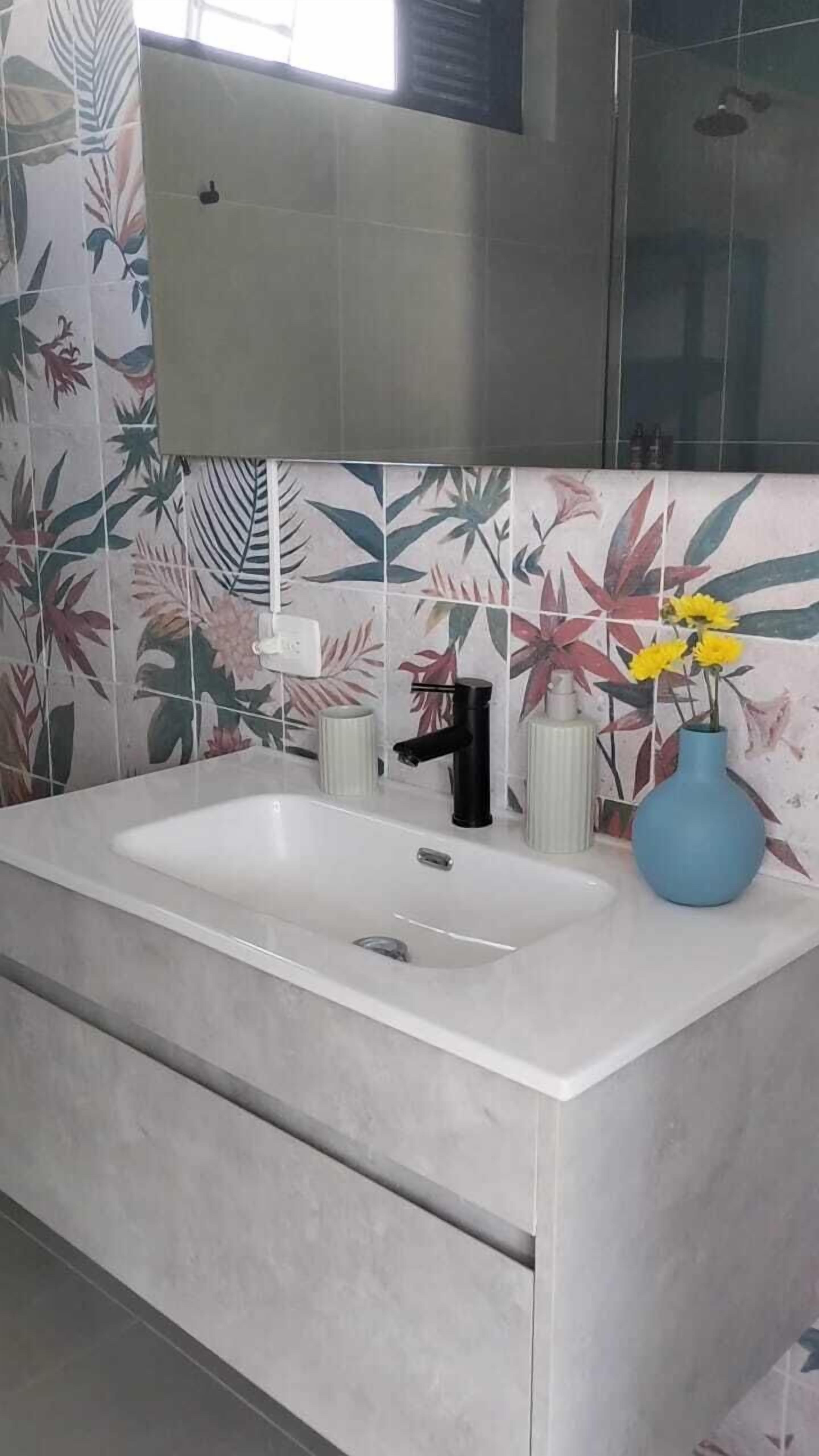 Une salle de bain avec un lavabo blanc, un robinet noir et un vase bleu contenant des fleurs jaunes.