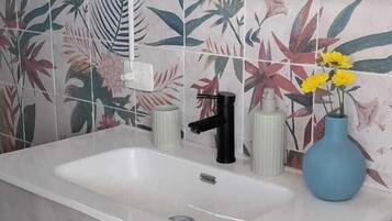 Een badkamer met een witte wastafel, een zwarte kraan en een blauwe vaas met gele bloemen.
