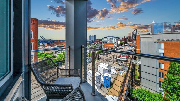 A balcony with wicker furniture, a city view, and a clear sky.