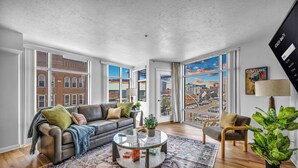 A spacious living room with a leather sofa, a glass coffee table, and a view of a cityscape through large windows.