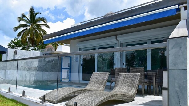 A modern outdoor pool area with lounge chairs, a glass-enclosed patio, and a view of the building's exterior. - Two private beachfront houses, sleeps 12, kayaks, private heated pools (Cabo Rojo)