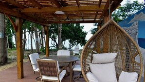 An outdoor patio with a round wooden table and white cushioned chairs, a wicker hanging chair, and a pergola structure. - Two private beachfront houses, sleeps 12, kayaks, private heated pools (Cabo Rojo)