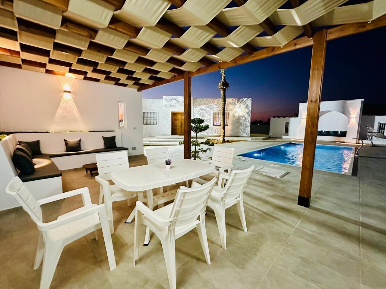 Une terrasse extérieure avec une table et des chaises blanches, une piscine et une pergola en bois.