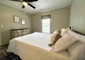 Un dormitorio con cama, cómoda, ventilador de techo y ventana.