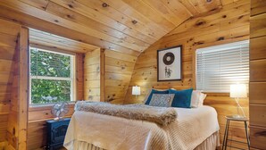Une chambre confortable dans un chalet en bois, avec un lit, une fenêtre avec des stores, un tableau accroché au mur et une petite table avec une lampe.
