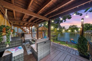 A covered outdoor seating area with wicker furniture, a view of a lake, and string lights.
