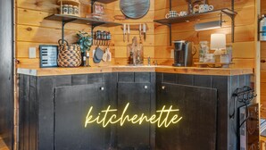 Une cuisine avec des murs en bois, des étagères remplies d’ustensiles de cuisine et un néon indiquant « kitchenette ».