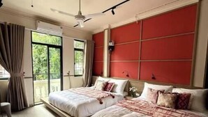 A modern hotel room with two beds, a large window, and a red accent wall.