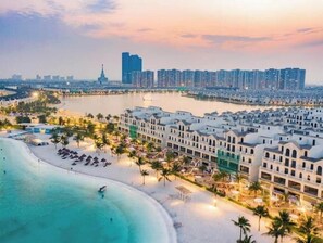 Ein Küstenhotel mit direktem Strandzugang, einer Marina und Hochhäusern im Hintergrund.