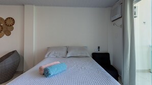 A bedroom with a bed, pillows, a bedside table, a lamp, and a wall-mounted air conditioner. - Loft com Varanda e Vista Para o mar em Mangaratiba (Mangaratiba)