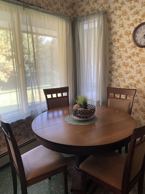 A round wooden dining table with four chairs, a woven basket with a plant, and a wall clock.