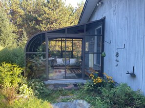 A modern house with a glass-enclosed porch, a wooden exterior, and a garden with various plants and flowers.