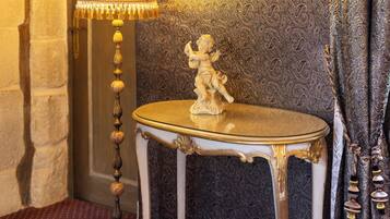 A room with a patterned wall, a round mirror, a lamp, and a small table with a statue.