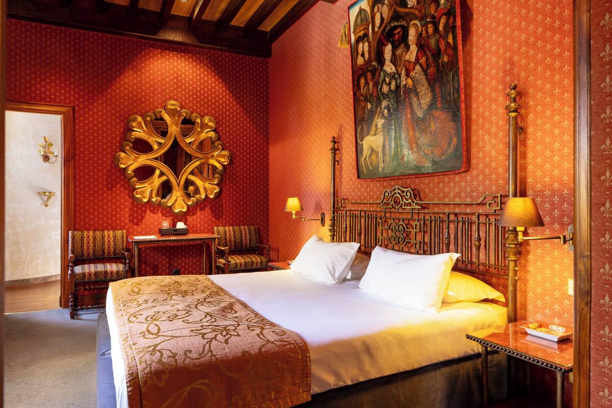 Habitación de hotel con una cama grande, un espejo decorativo, un cuadro en la pared y un cabecero de madera.
