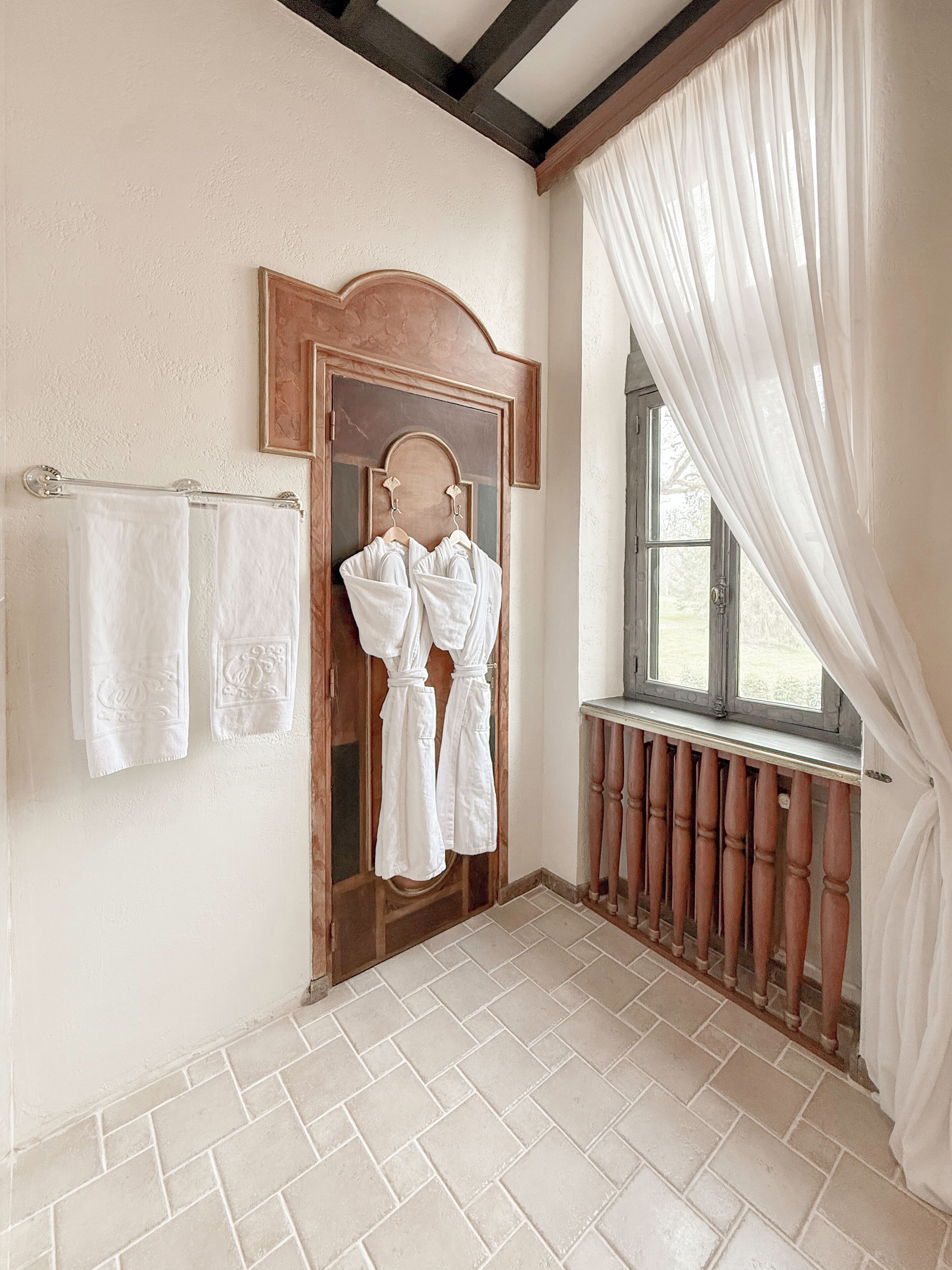 Ein Badezimmer mit Holztür, weißen Handtüchern und einem Fenster mit Vorhängen.