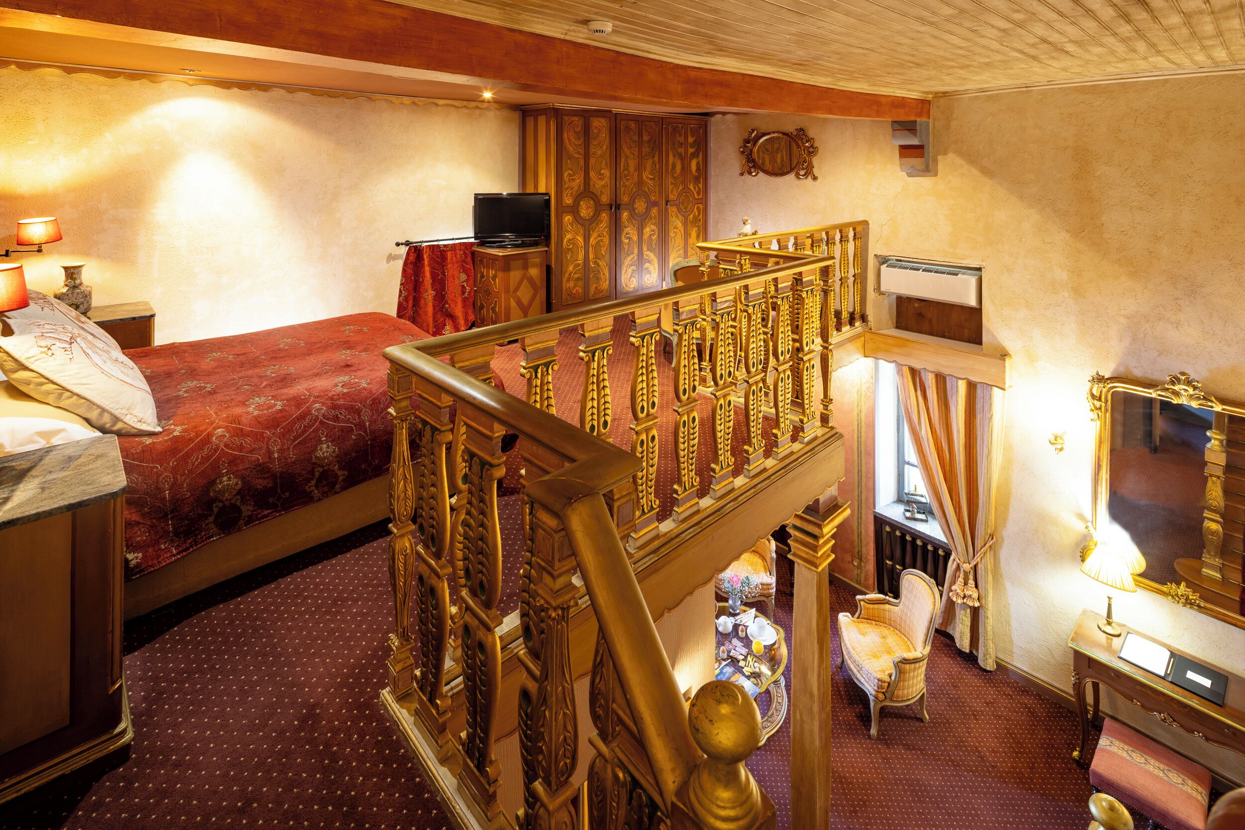 A room with a bed, a television, a wooden staircase, and a mirror.