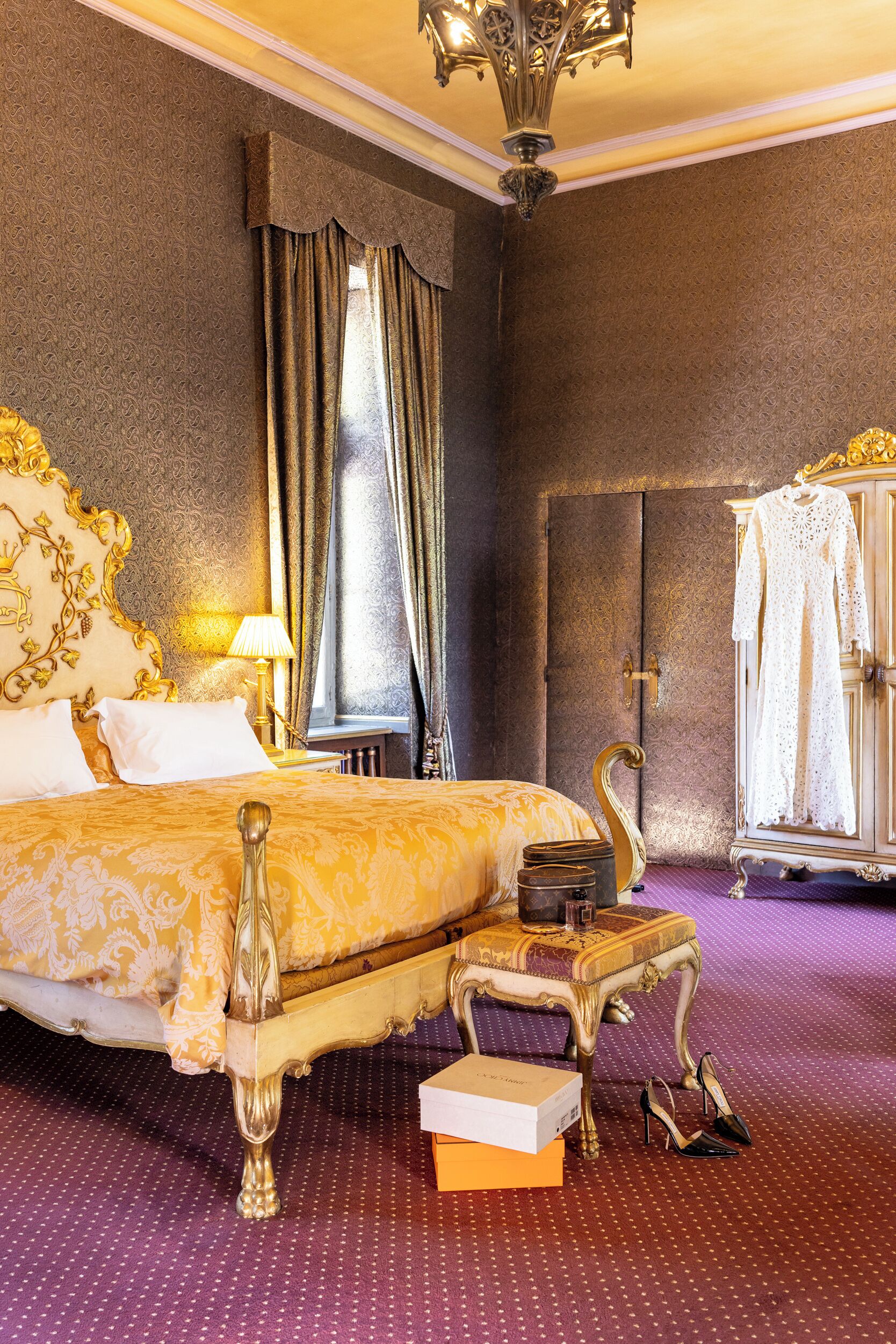 A luxurious hotel room with a large bed, ornate headboard, a vanity with a mirror, and a wardrobe.