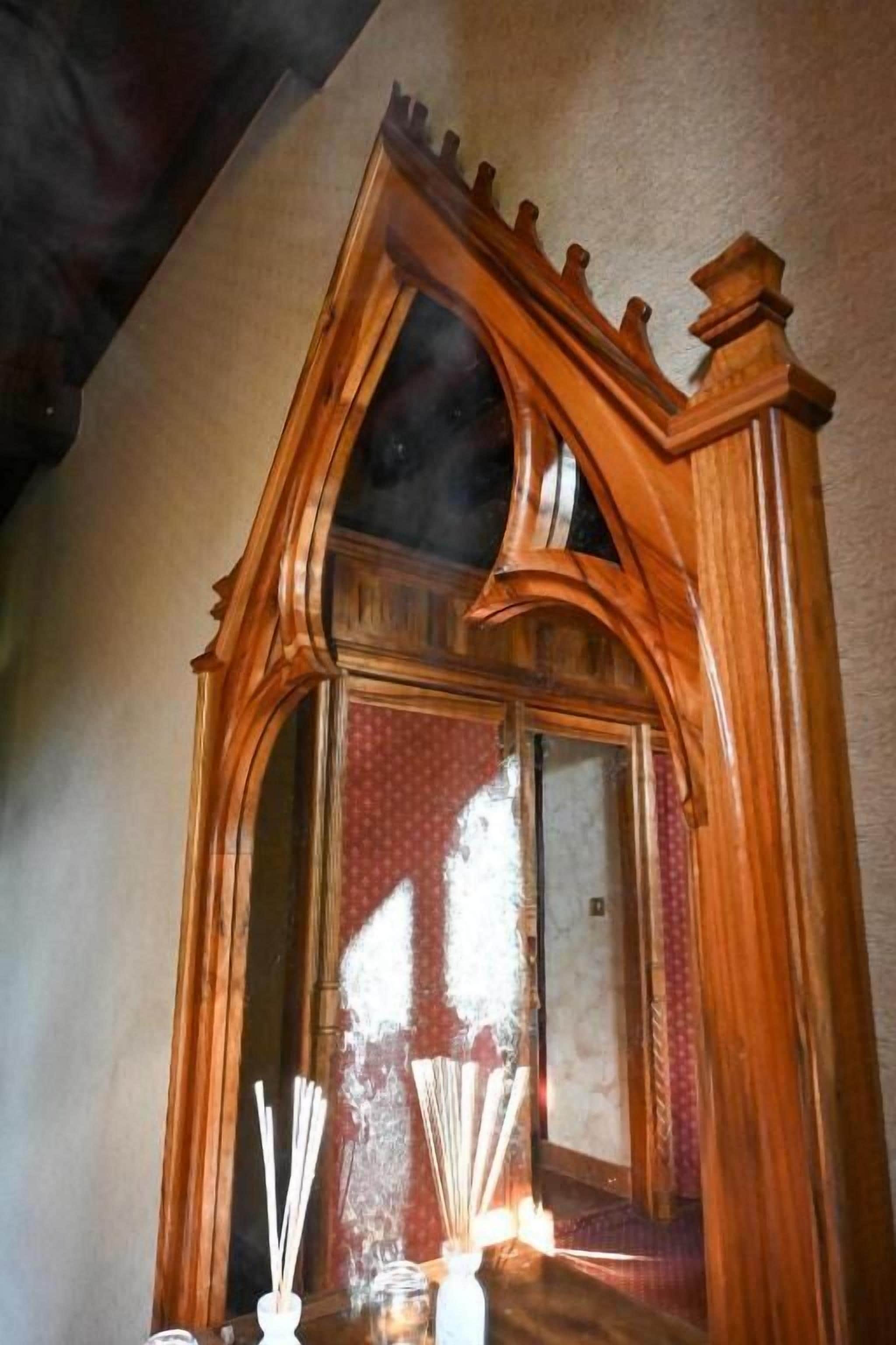 Un espejo arqueado de madera con un marco decorativo, un florero con difusores de aroma y un papel tapiz estampado al fondo.