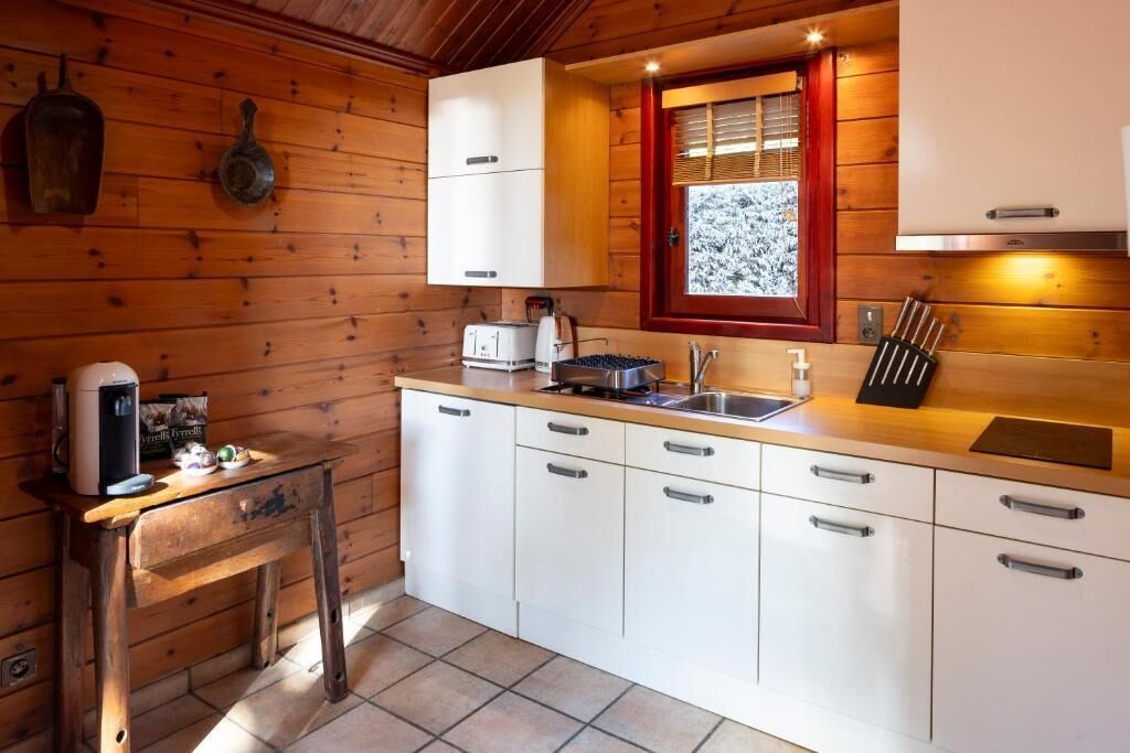 A compact kitchen with white cabinets, a wooden countertop, a window with a view of snow-covered trees, and a coffee machine.
