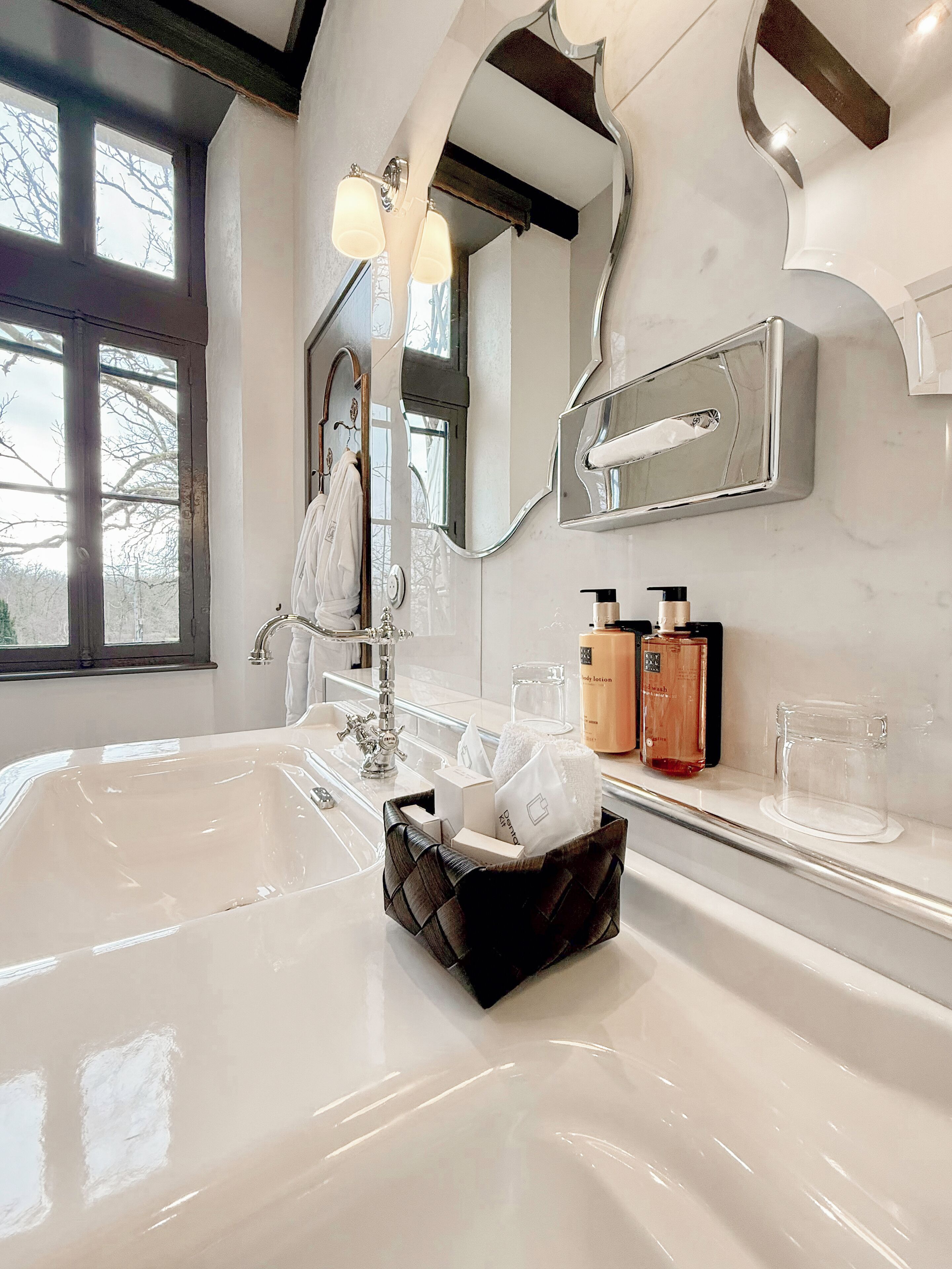 A bathroom with a large mirror, a bathtub, and a vanity with toiletries.