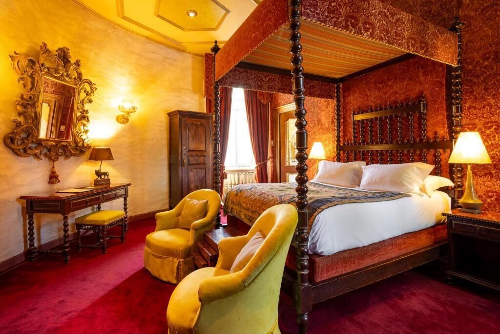 A four-poster bed with a canopy, a large ornate mirror, and two armchairs.